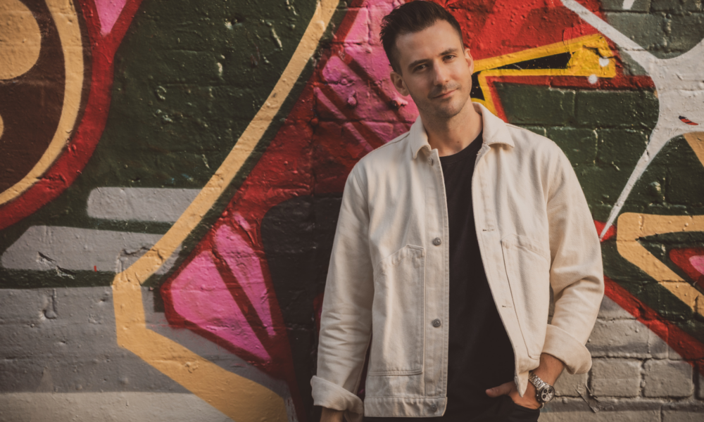 Stefan Rose standing in front of a graffiti wall wearing a white jacket for his latest single Closing In release via Music is 4 Lovers.
