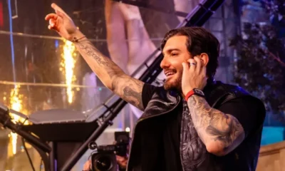 Alesso smiling and pointing to the crowd while DJing on stage with warm stage lighting behind him