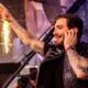 Alesso smiling and pointing to the crowd while DJing on stage with warm stage lighting behind him