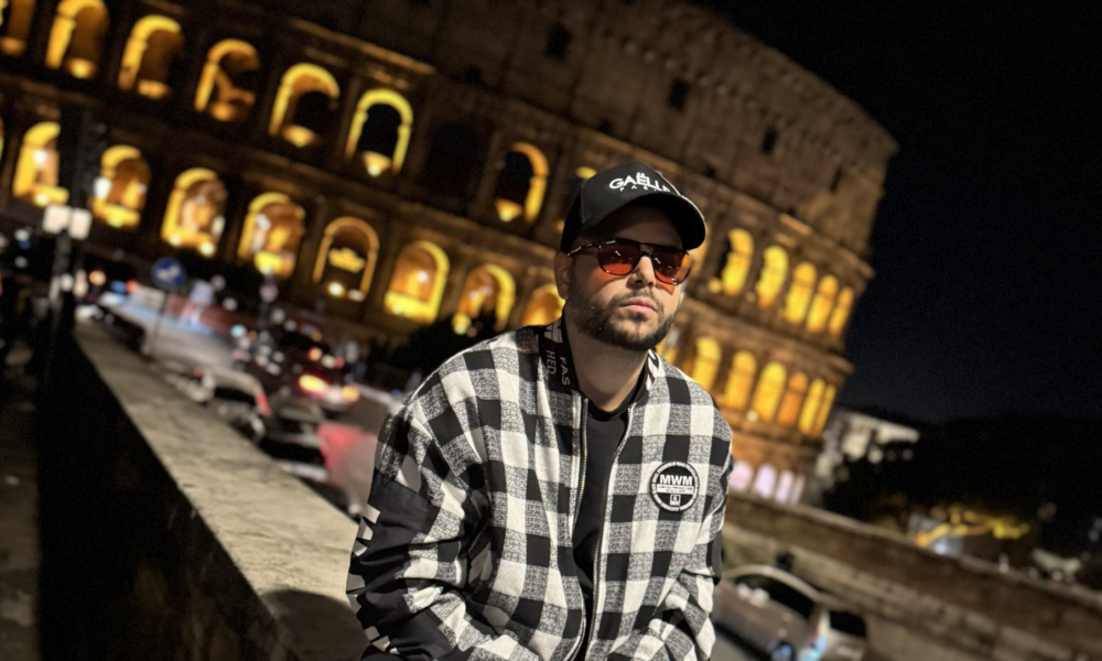 Danny Eviza sitting on a wall with a laptop in front of the illuminated Colosseum at night