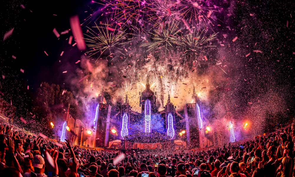 Purple and gold fireworks exploding above the Electrisize Mainstage as confetti rains down over the crowd