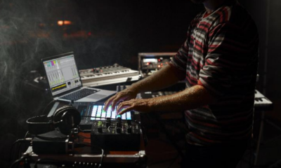 An electronic music artist using a laptop with performance software, a MIDI pad controller, mixer, and keyboard during a live performance.