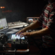An electronic music artist using a laptop with performance software, a MIDI pad controller, mixer, and keyboard during a live performance.