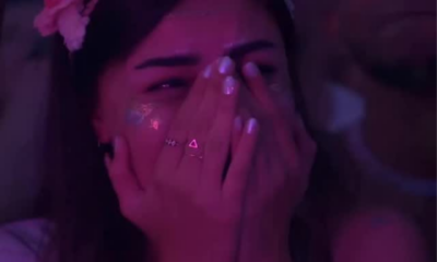 A woman covering her face while crying during a DJ set under purple festival lighting.