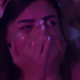 A woman covering her face while crying during a DJ set under purple festival lighting.