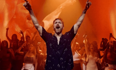 David Guetta performing at Galactic Circus at [UNVRS] Ibiza with both arms raised as orange visuals fill the stage behind him.