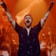 David Guetta performing at Galactic Circus at [UNVRS] Ibiza with both arms raised as orange visuals fill the stage behind him.