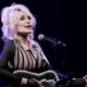 Dolly Parton singing into a microphone while playing guitar on stage