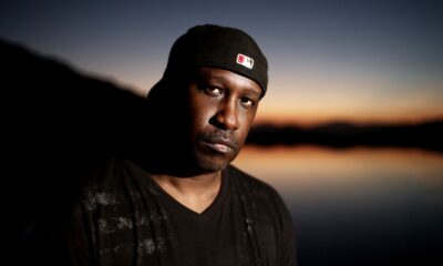 Todd Terry wearing a black beanie, standing against a sunset sky over water
