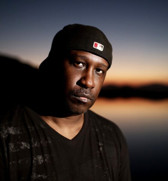 Todd Terry wearing a black beanie, standing against a sunset sky over water