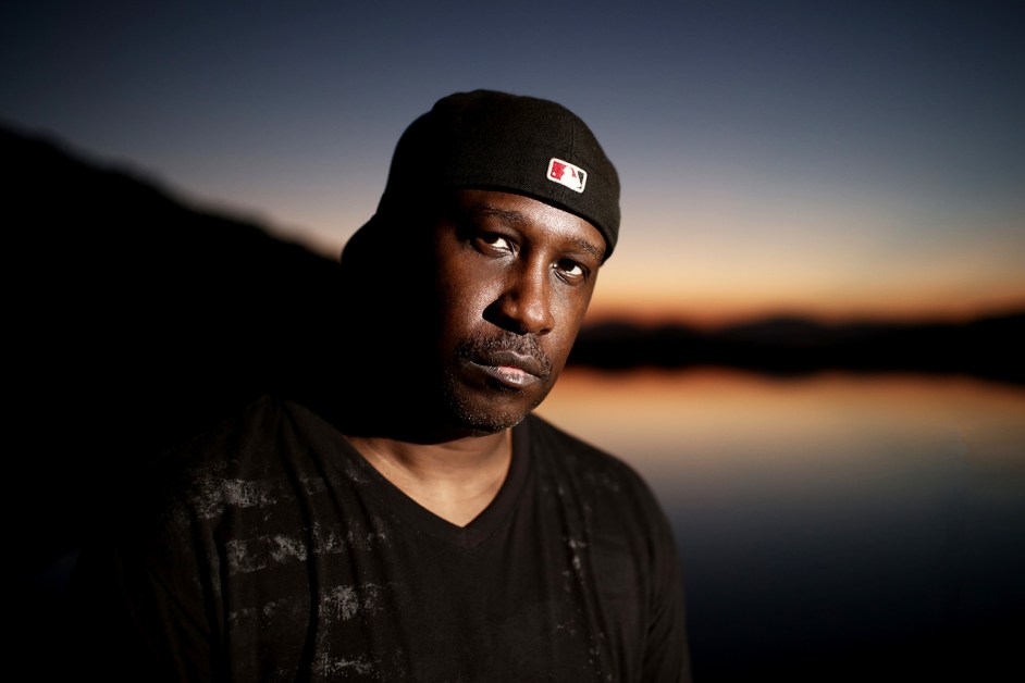 Todd Terry wearing a black beanie, standing against a sunset sky over water