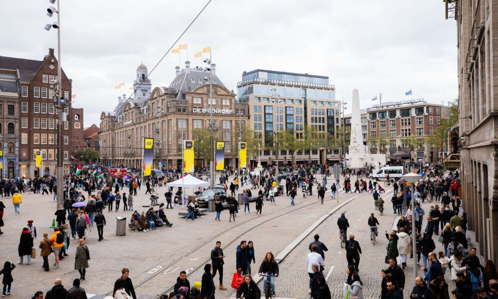 Crowds gathered in Dam Square in Amsterdam with yellow ADE banners visible on lampposts during Amsterdam Dance Event