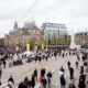 Crowds gathered in Dam Square in Amsterdam with yellow ADE banners visible on lampposts during Amsterdam Dance Event