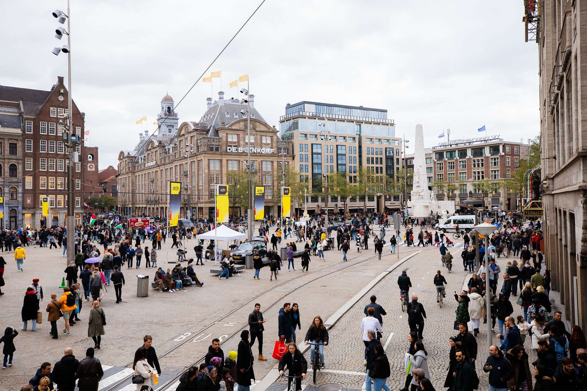 Crowds gathered in Dam Square in Amsterdam with yellow ADE banners visible on lampposts during Amsterdam Dance Event