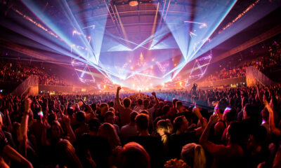 Crowd at Amsterdam Dance Event dancing under blue and purple laser lights inside a packed arena