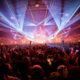 Crowd at Amsterdam Dance Event dancing under blue and purple laser lights inside a packed arena