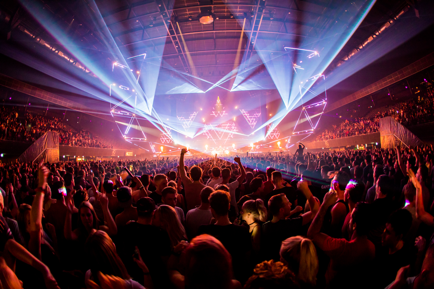 Crowd at Amsterdam Dance Event dancing under blue and purple laser lights inside a packed arena
