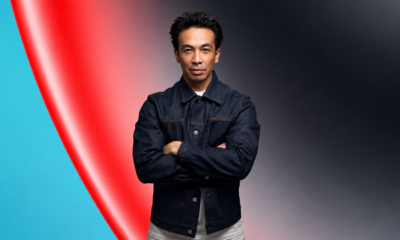 Laidback Luke wearing a denim jacket with arms crossed against a red and teal abstract background