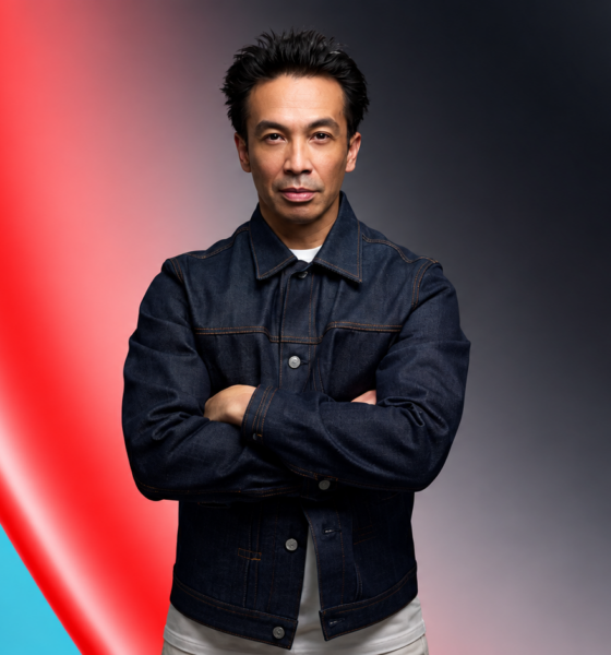 Laidback Luke wearing a denim jacket with arms crossed against a red and teal abstract background