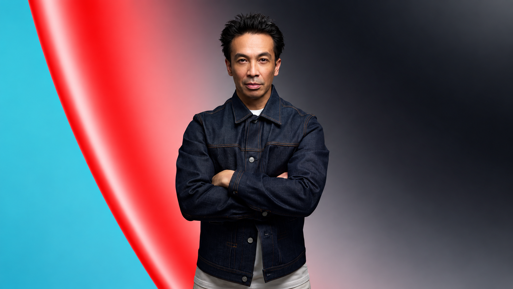 Laidback Luke wearing a denim jacket with arms crossed against a red and teal abstract background