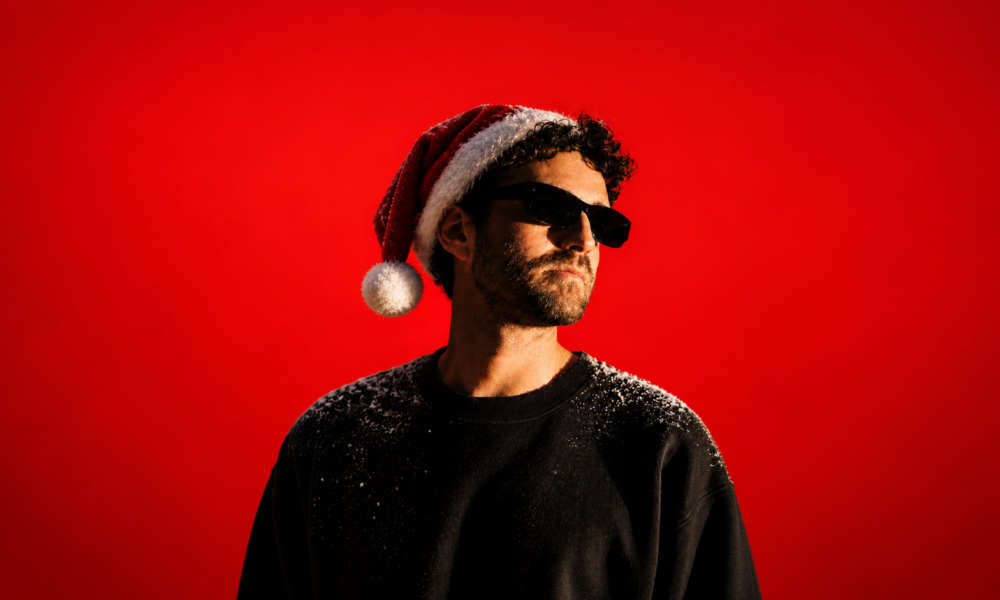 DJ wearing sunglasses and a Santa hat against a bright red background, dusted with snow on his shoulders