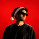 DJ wearing sunglasses and a Santa hat against a bright red background, dusted with snow on his shoulders