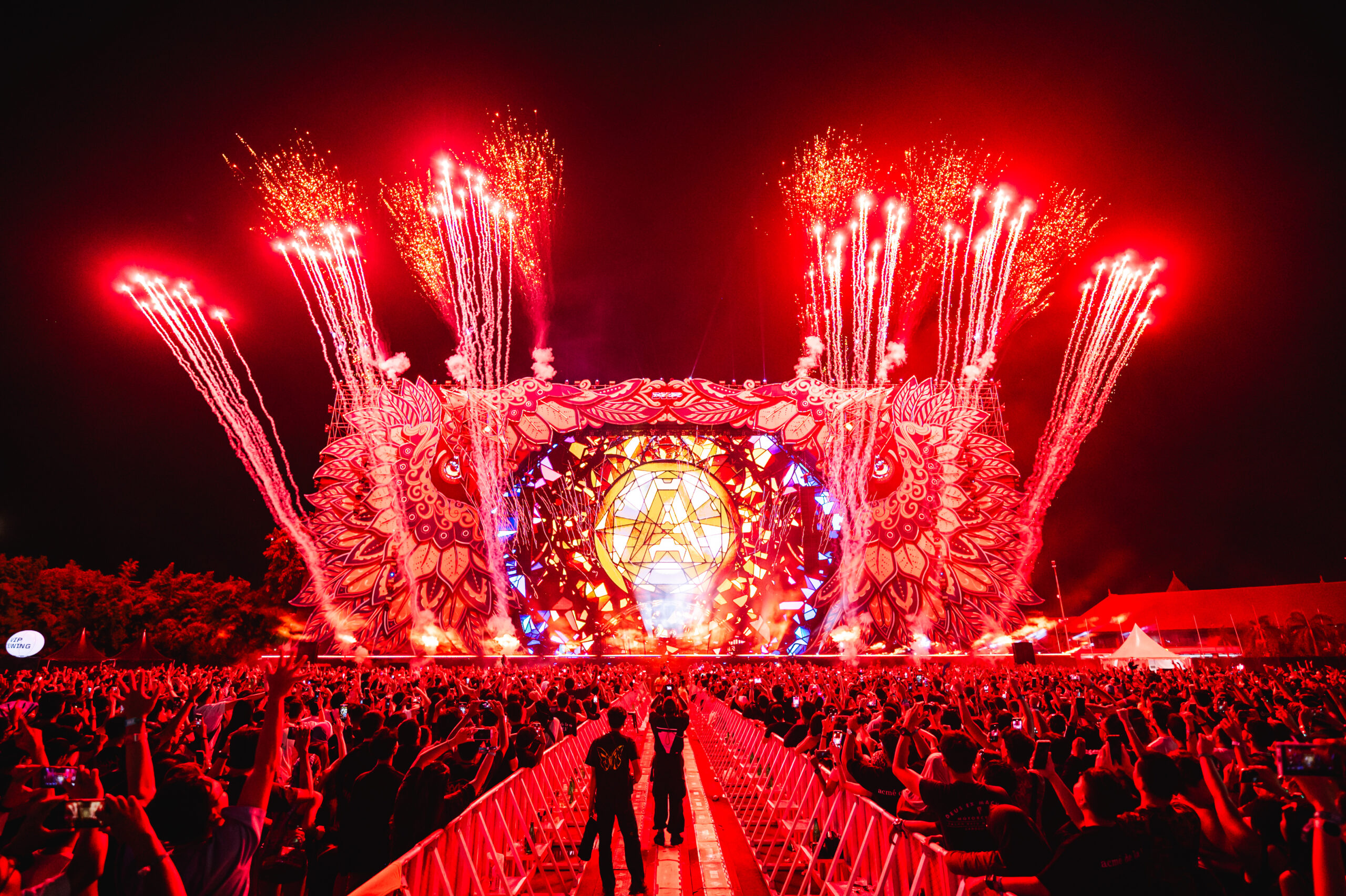 Red fireworks and pyrotechnics exploding above the Djakarta Warehouse Project (DWP) mainstage as the crowd raises their hands