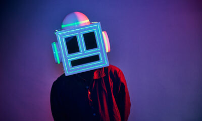 MEETCH wearing his LED-lit robot helmet and a red and black shirt against a purple backdrop
