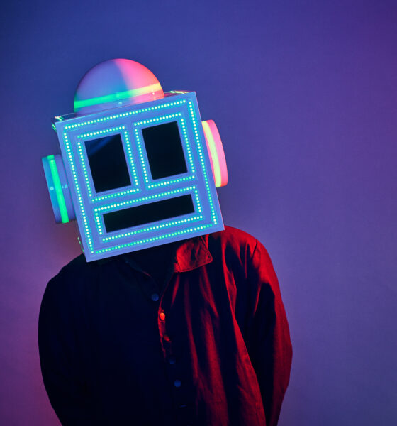 MEETCH wearing his LED-lit robot helmet and a red and black shirt against a purple backdrop