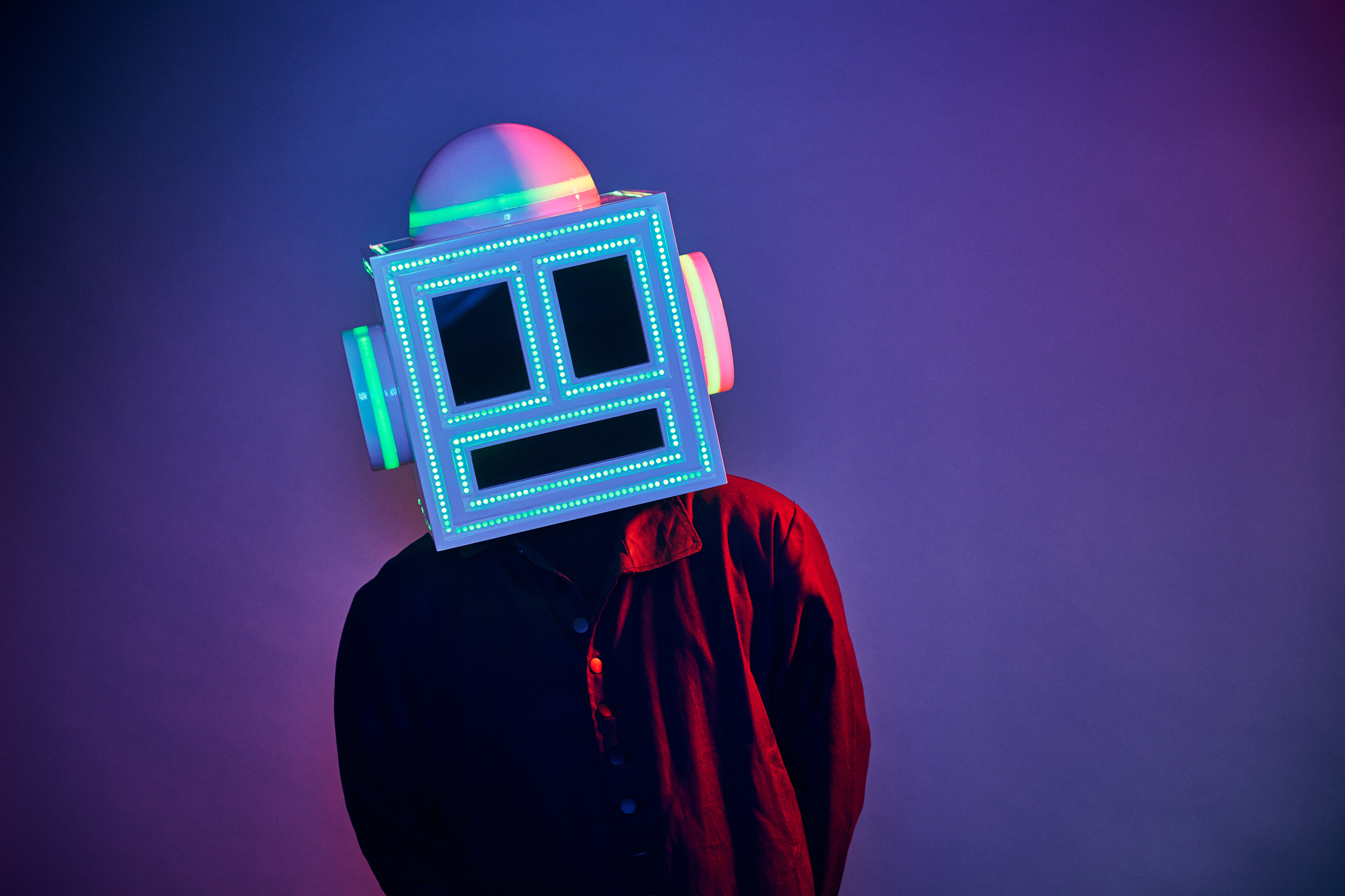 MEETCH wearing his LED-lit robot helmet and a red and black shirt against a purple backdrop