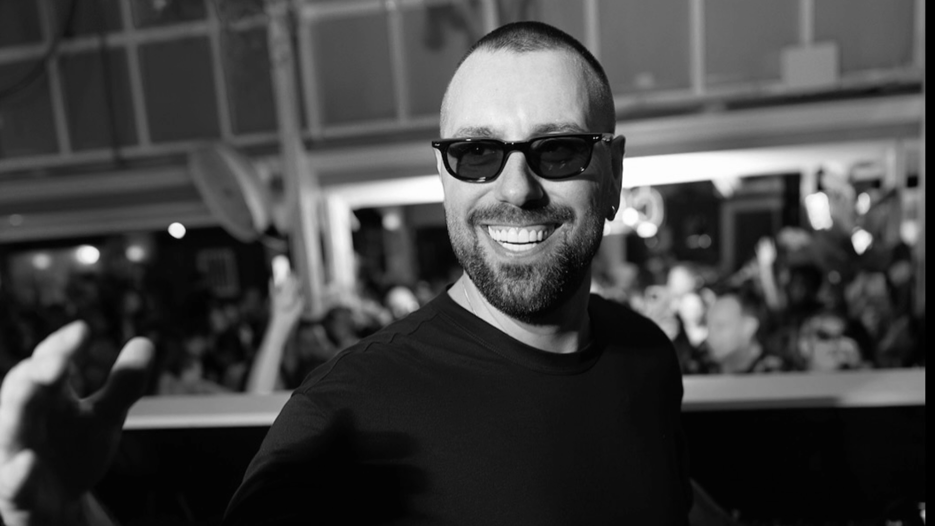 Black and white photo of Sebastian Ingrosso smiling and reaching toward the camera in front of a crowd