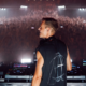 Armin van Buuren performing behind the decks in front of a large crowd during a live show at UNVRS