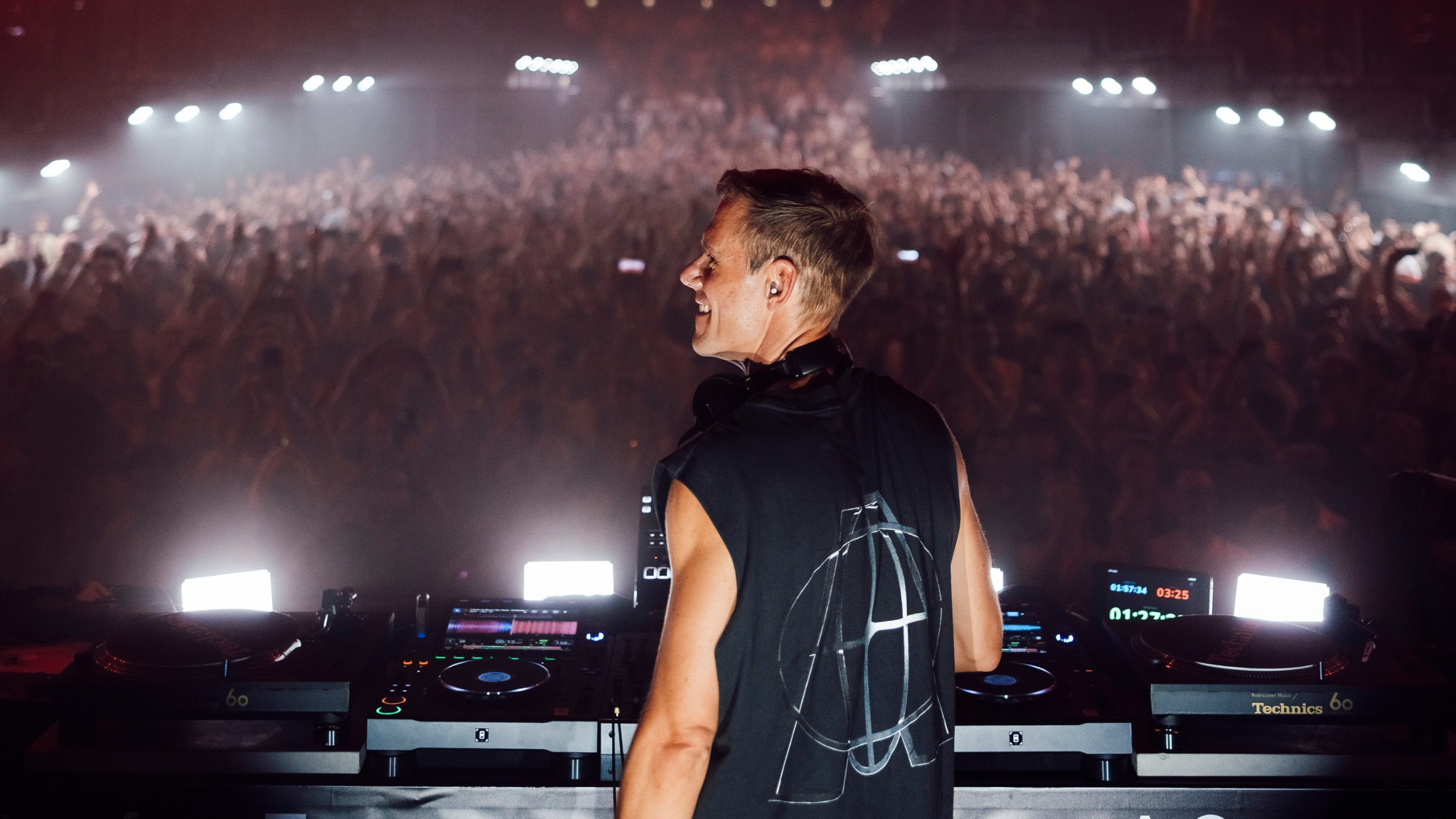 Armin van Buuren performing behind the decks in front of a large crowd during a live show at UNVRS