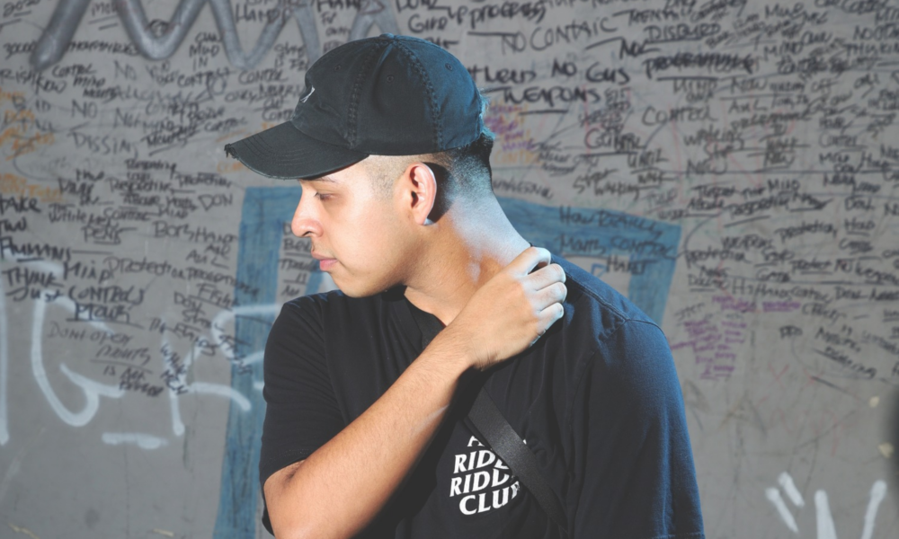 Deadlynoiz wearing a black cap and black shirt in front of a graffiti-covered wall