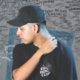 Deadlynoiz wearing a black cap and black shirt in front of a graffiti-covered wall