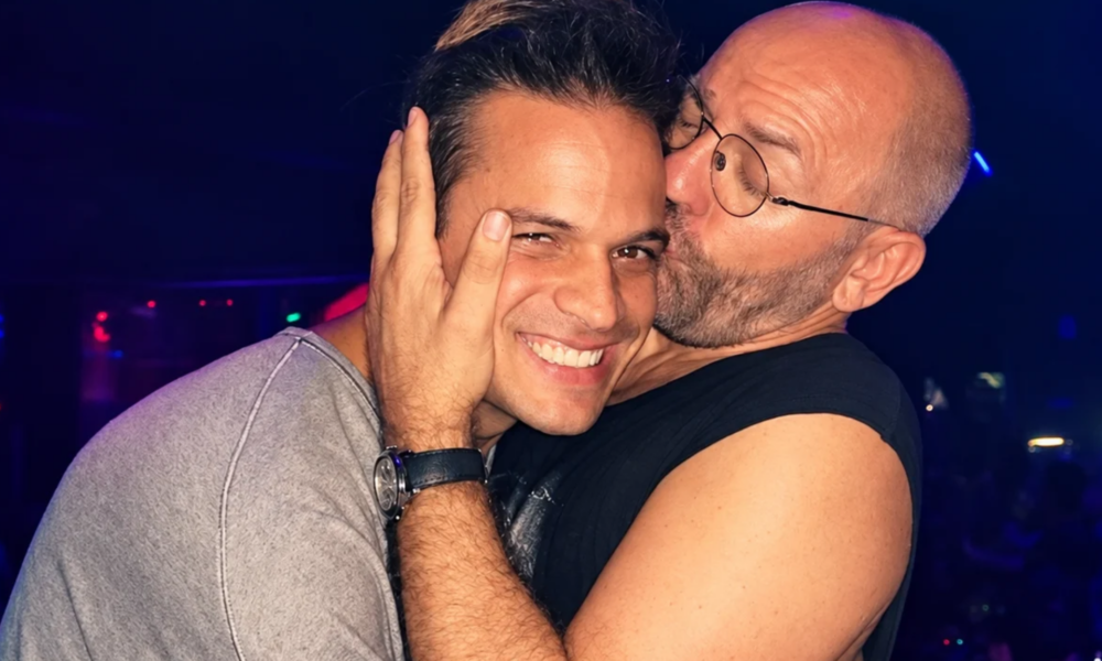 Argy smiling as Sven Väth kisses him on the cheek inside a nightclub