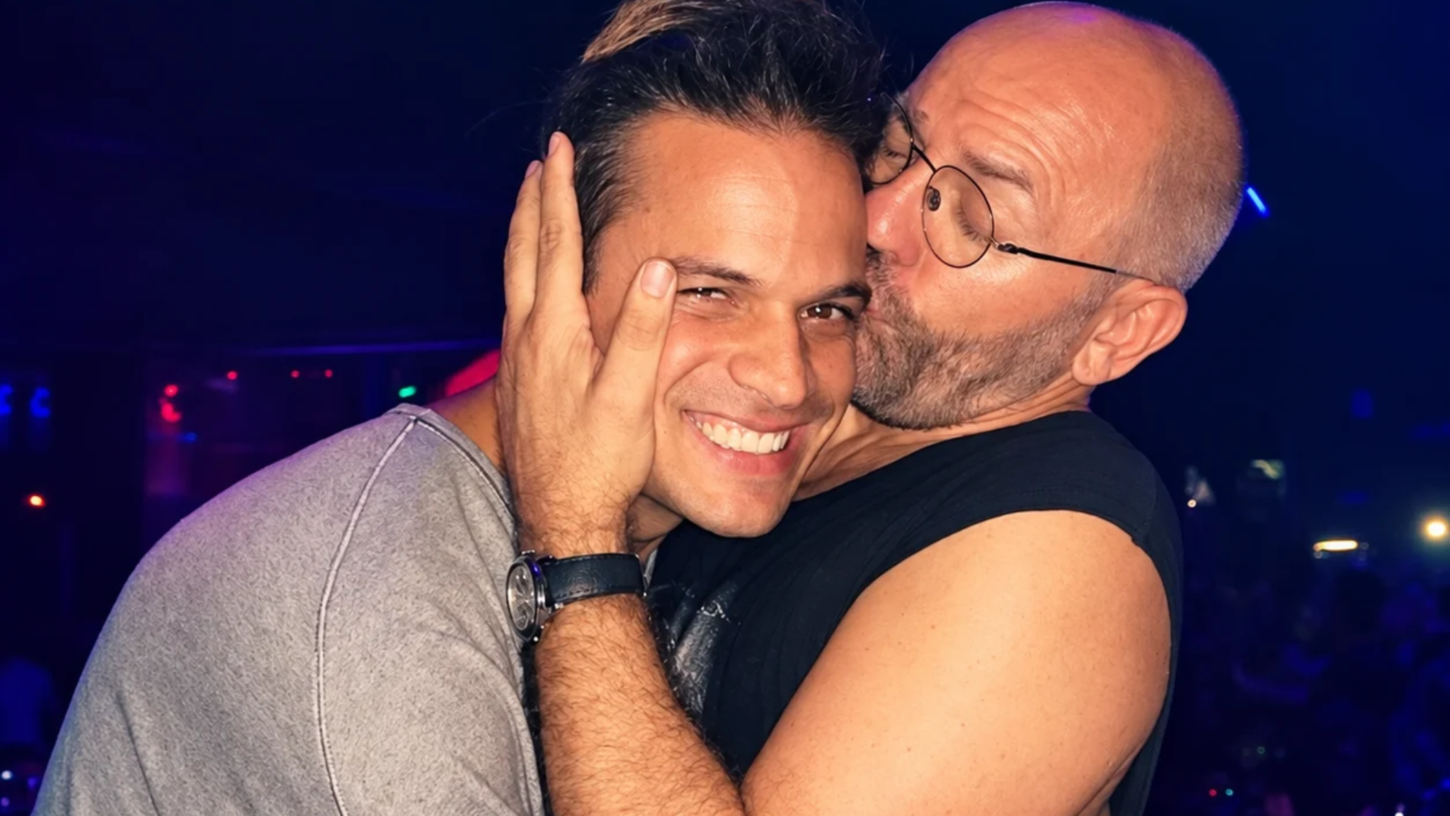 Argy smiling as Sven Väth kisses him on the cheek inside a nightclub