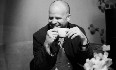 Black-and-white portrait of a man smiling while holding a cup, used for Roland Leesker’s ‘What You Need’ release on Definitive Recordings