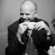 Black-and-white portrait of a man smiling while holding a cup, used for Roland Leesker’s ‘What You Need’ release on Definitive Recordings
