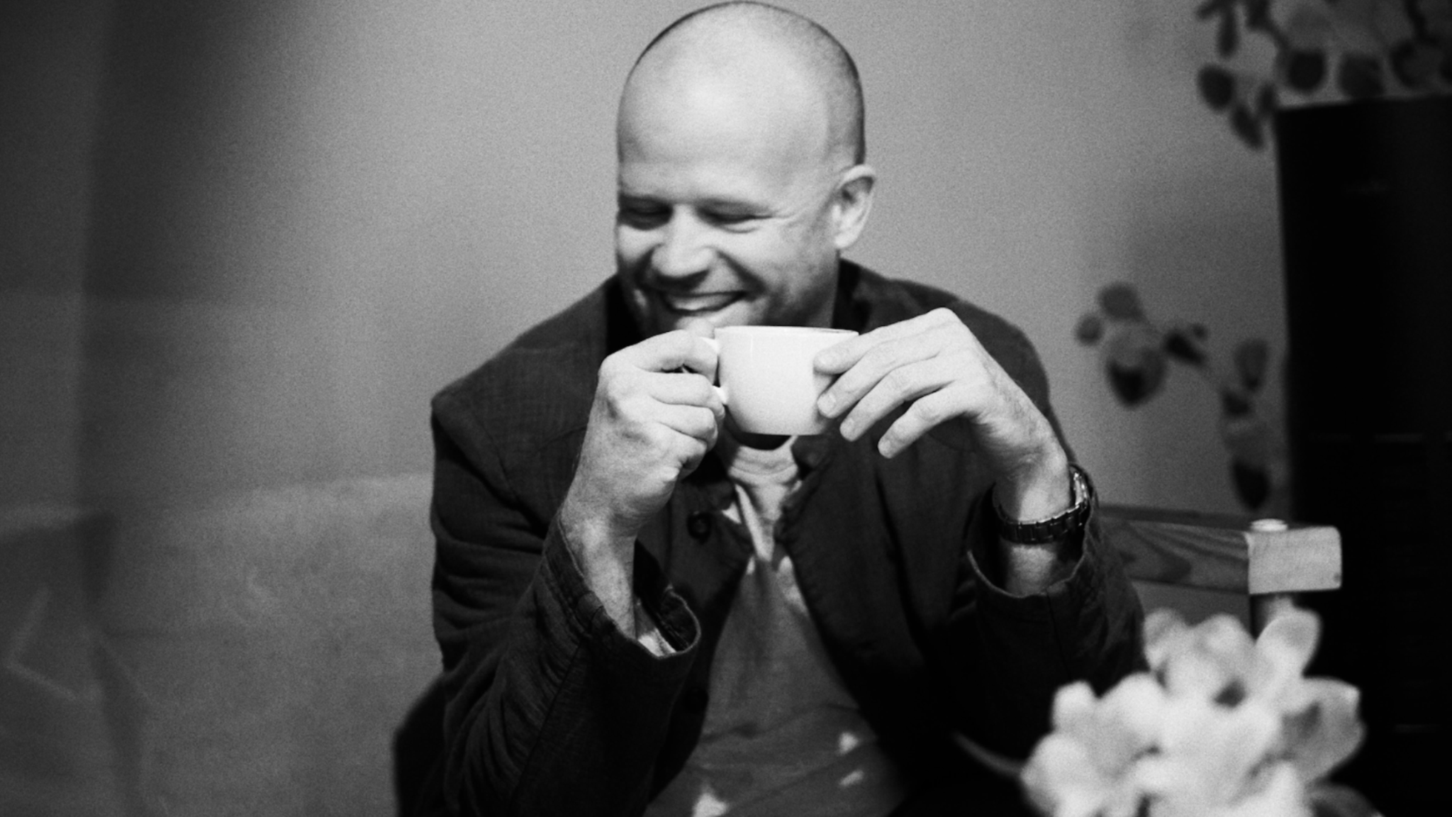 Black-and-white portrait of a man smiling while holding a cup, used for Roland Leesker’s ‘What You Need’ release on Definitive Recordings