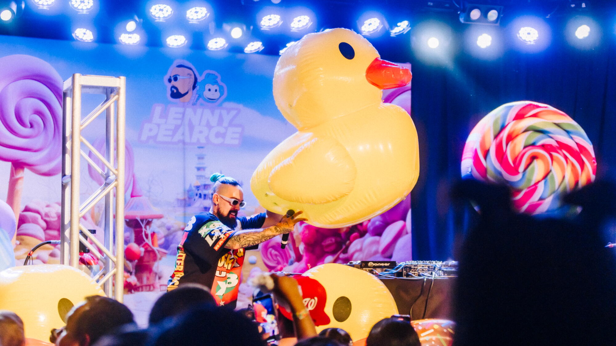 Lenny Pearce performing at a baby rave with a giant inflatable duck, colorful stage decorations and families watching from the crowd