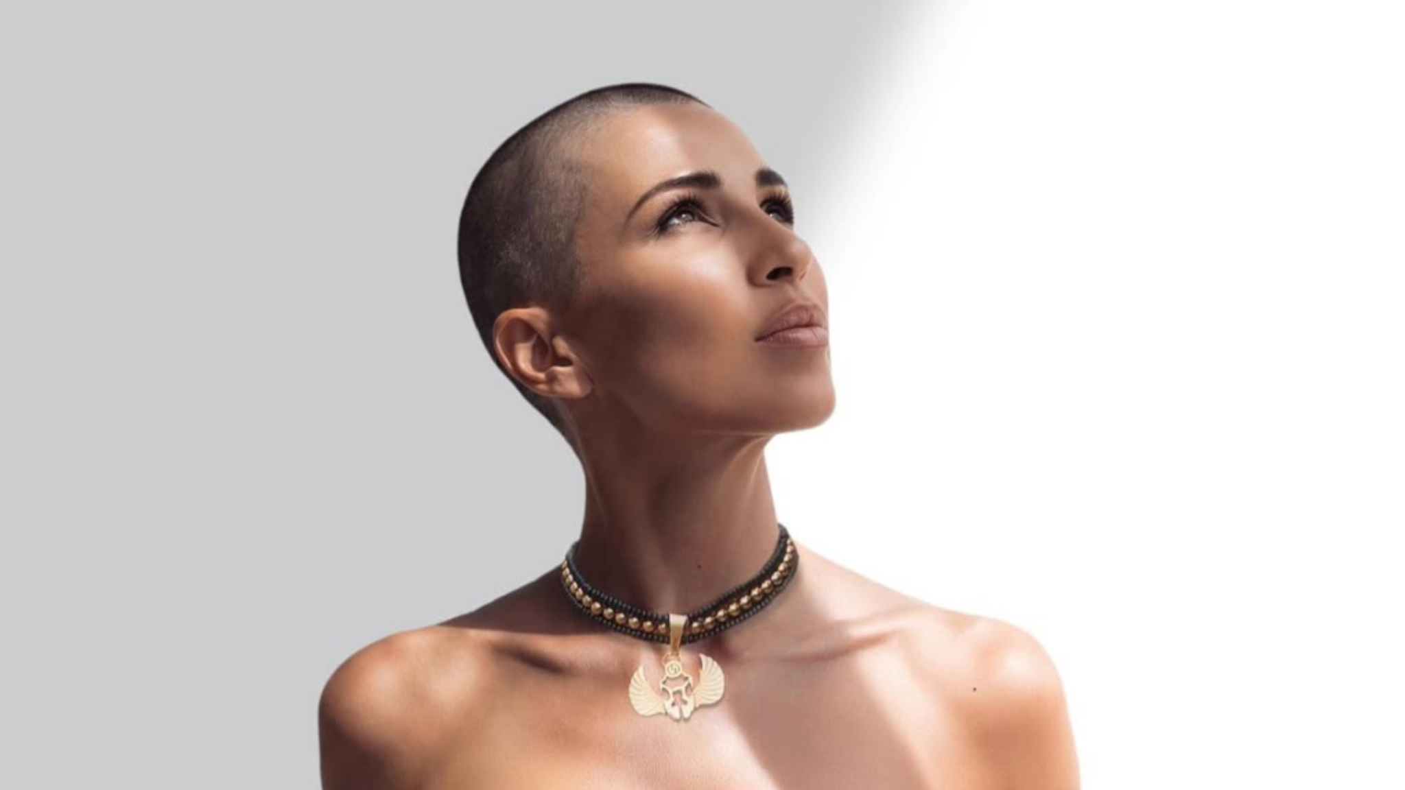 Portrait of B Jones with a shaved head looking upward against a light grey and white background.