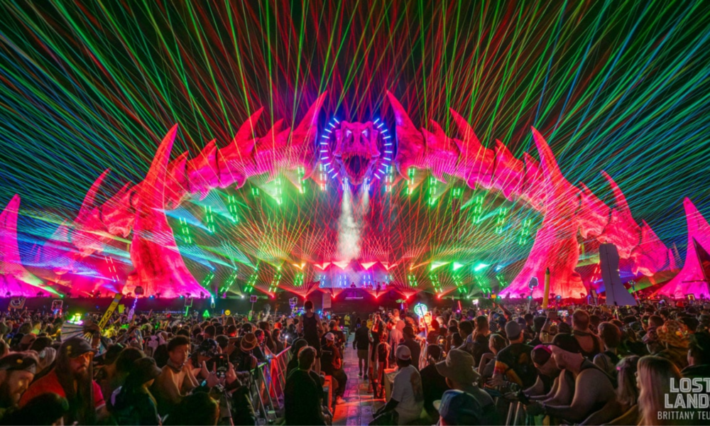 Lost Lands stage illuminated by colorful lasers as a large crowd watches the performance at Legend Valley