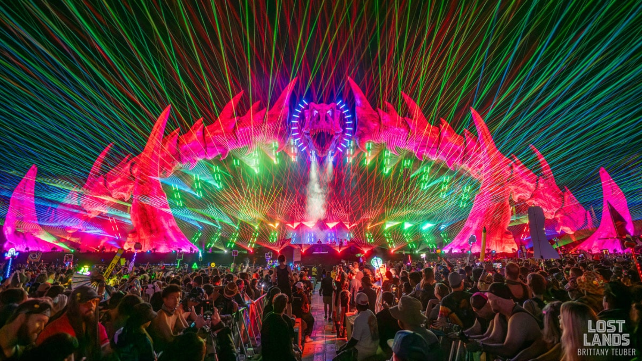 Lost Lands stage illuminated by colorful lasers as a large crowd watches the performance at Legend Valley