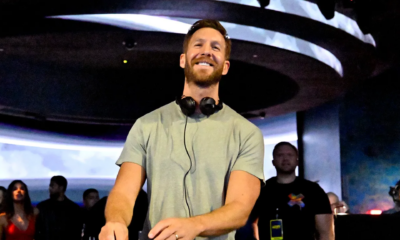 Calvin Harris smiling behind the decks with headphones around his neck during a live performance