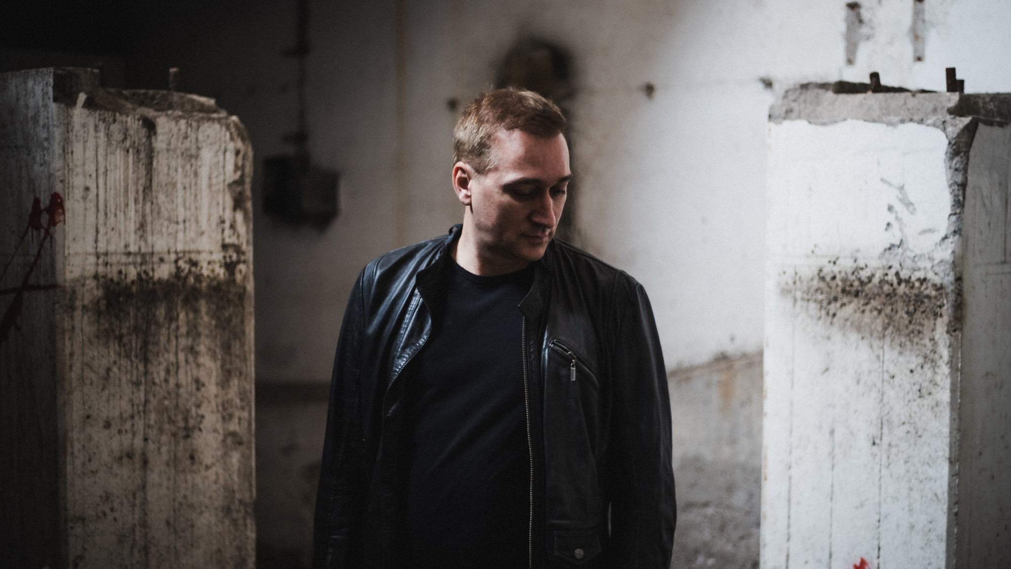 Paul van Dyk wearing a black leather jacket inside an industrial concrete setting ahead of The Essence of Acid live show.