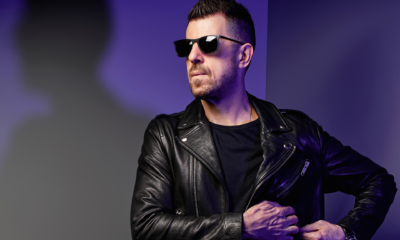 Sgt Slick wearing black sunglasses and a leather jacket in a purple-lit promotional portrait for his Strings Of Life remix
