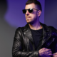 Sgt Slick wearing black sunglasses and a leather jacket in a purple-lit promotional portrait for his Strings Of Life remix