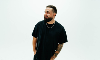 : HEYZ smiling in a black T-shirt and silver chain against a white background