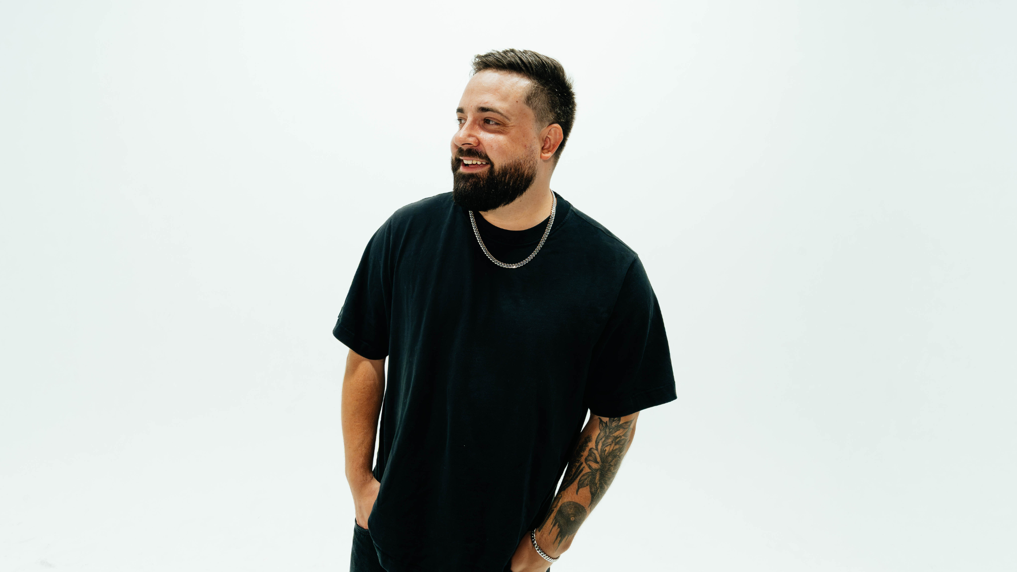 : HEYZ smiling in a black T-shirt and silver chain against a white background